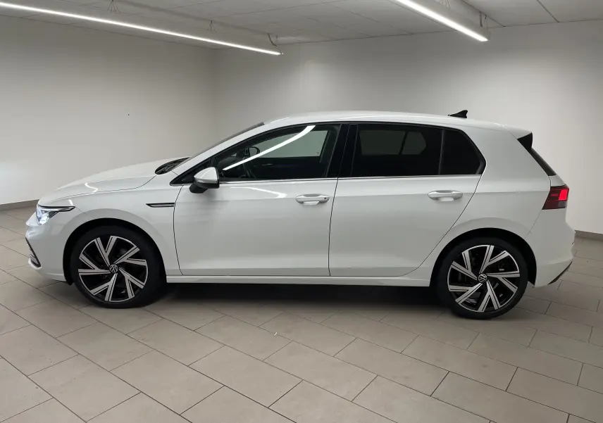 Profil côté gauche d'une Volkswagen Golf 1.5 eTSI Style blanche avec jantes Bergamo et vitres arrière surteintées.
