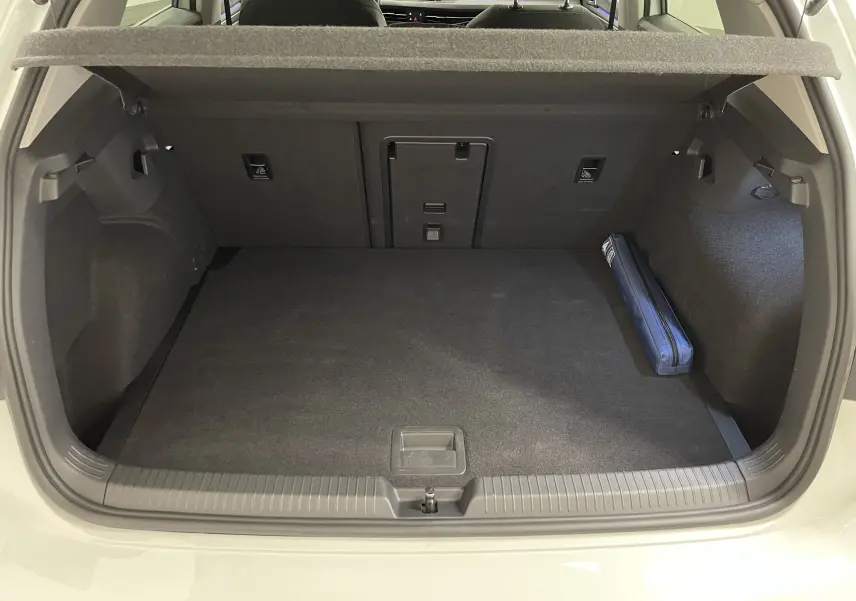 Coffre ouvert d'une Volkswagen Golf blanche, vue arrière montrant un espace de chargement propre avec trousse bleue sur le côté droit.