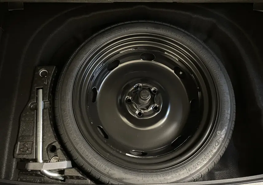 Gros plan sur la roue de secours à encombrement réduit et le cric dans le coffre d'une Volkswagen Golf blanche 2023.