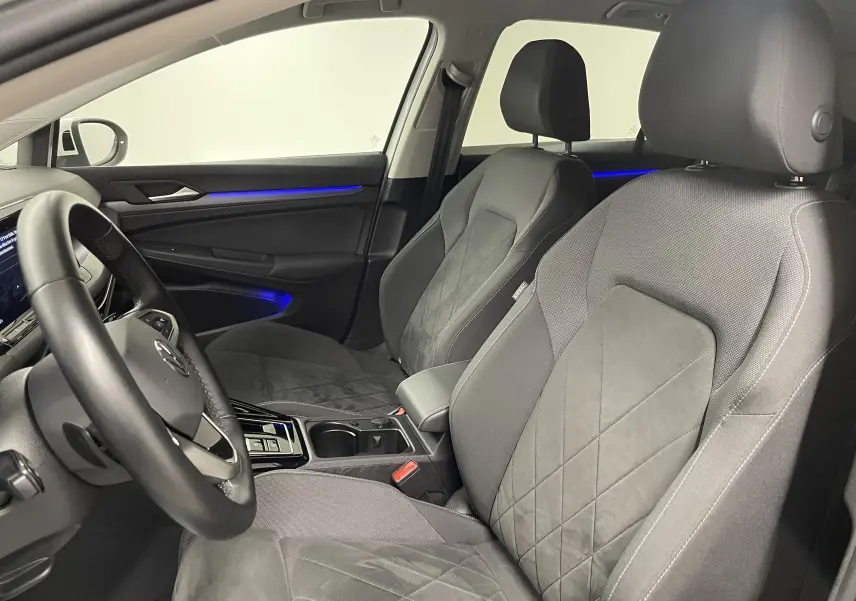 Vue intérieure côté conducteur de la Volkswagen Golf 1.5 eTSI 2023 avec sièges tissu gris et éclairage d'ambiance bleu.