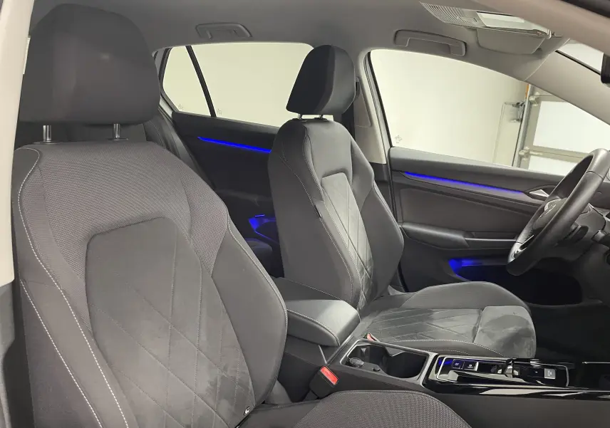 Intérieur de la Volkswagen Golf blanc pur 2023, vue côté droit sur les sièges avant et éclairage d'ambiance bleu.
