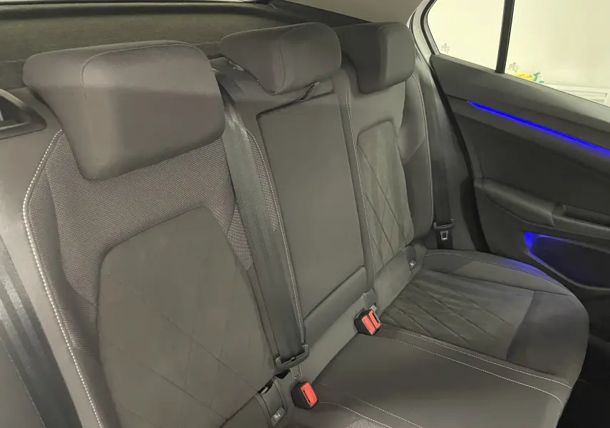 Vue intérieure des sièges arrière noirs de la Volkswagen Golf 1.5 eTSI 2023 avec éclairage d'ambiance bleu sur la porte droite