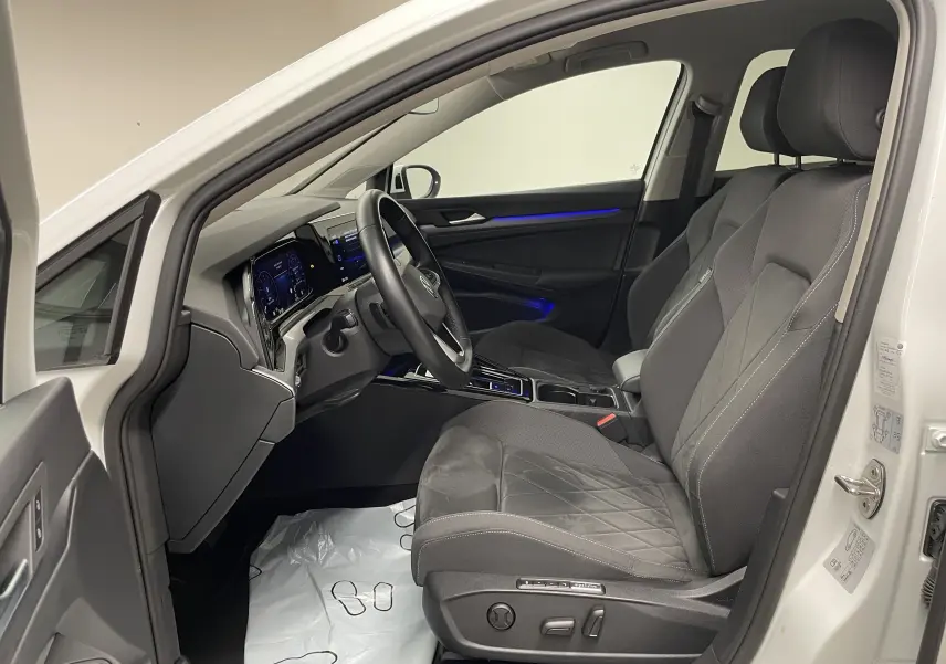 Intérieur avant droit d'une Volkswagen Golf blanche 2023, sièges noirs avec surpiqûres et éclairage d'ambiance bleu
