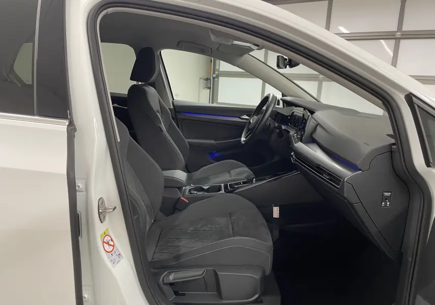 Intérieur de la Volkswagen Golf 1.5 eTSI Style 2023 en blanc pur, vue côté gauche avec sièges noirs et éclairage d'ambiance bleu.