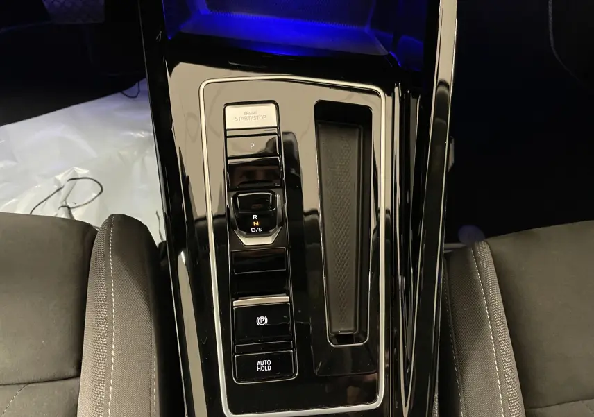 Vue rapprochée de la console centrale noire brillante avec commandes de boîte auto et frein à main électrique d'une Volkswagen Golf blanche.