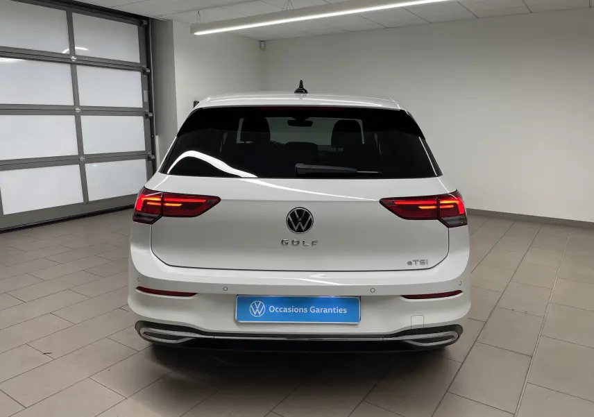 Vue arrière d'une Volkswagen Golf 1.5 eTSI blanche avec vitres arrière surteintées et feux allumés en intérieur.