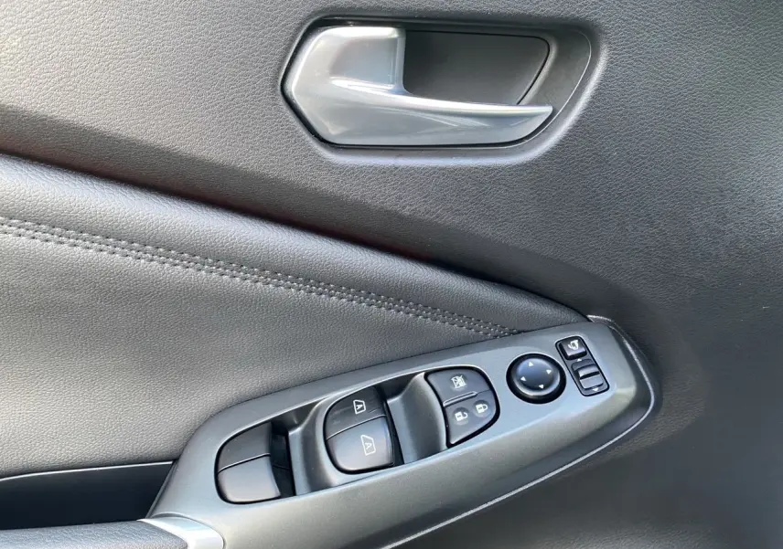 Détail de la porte intérieure côté conducteur du Nissan Juke 2025 en tissu noir avec commandes des vitres et poignée argentée.