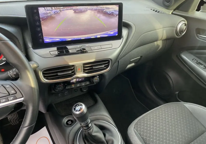 Vue intérieure côté passager du tableau de bord et console centrale du Nissan Juke 2025, avec écran tactile et sellerie tissu noir.