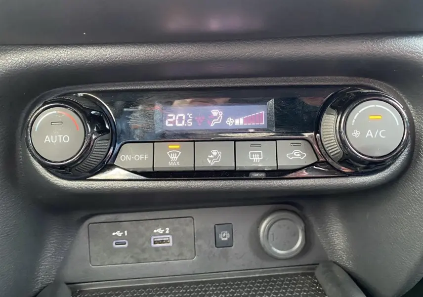 Gros plan sur la commande de climatisation automatique et ports USB du Nissan Juke 2025, intérieur noir.