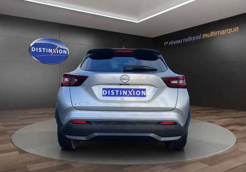 Vue arrière d'un Nissan Juke 2025 gris perle avec toit noir et feux LED, sur fond showroom Distinxion.