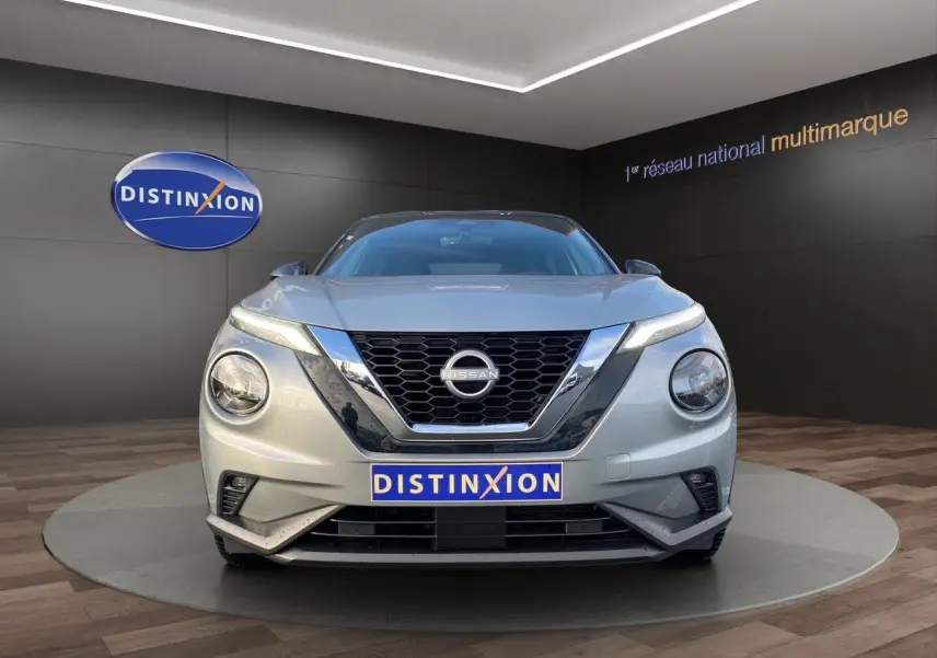 Vue avant d'un Nissan Juke 2025 gris perle avec toit noir, calandre en V chromée et phares ronds LED.