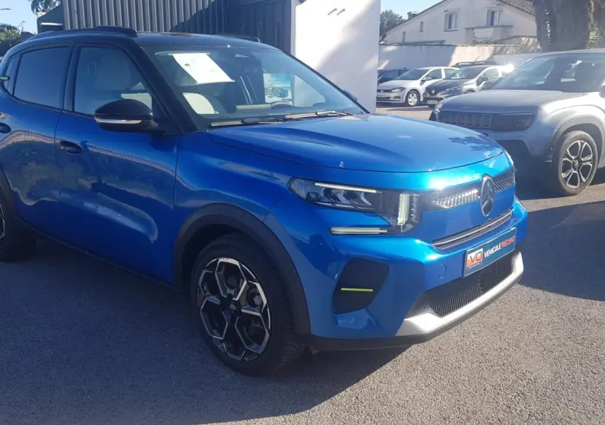 Vue 3/4 avant d'une Citroën C3 bleu foncé avec jantes alliage noires et barres de toit visibles en extérieur.