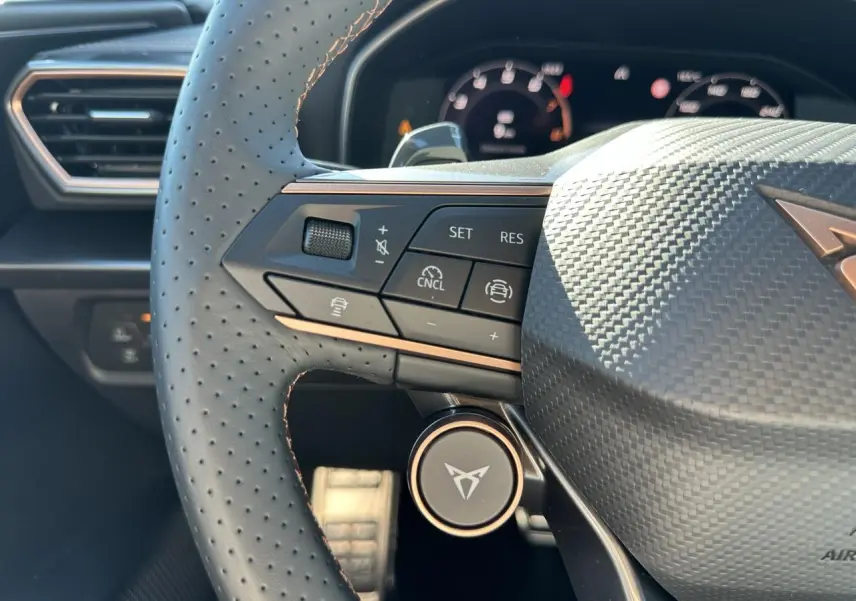 Gros plan sur le volant perforé noir avec logo CUPRA et commandes multifonctions dans l'habitacle du Leon Sportstourer.