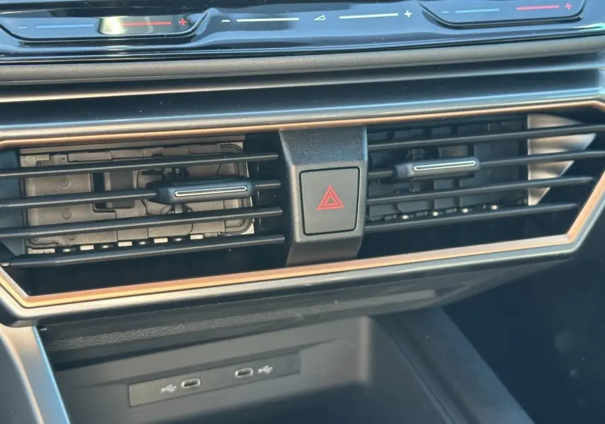 Gros plan sur la console centrale du CUPRA Leon Sportstourer 2025, avec aérateurs noirs et cadre cuivré, boutons tactiles rouges.