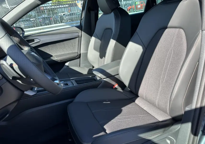 Intérieur de la CUPRA Leon Sportstourer 2025, vue côté conducteur sur sièges sports bimatière noirs et accoudoir central.