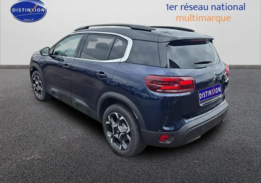 Vue 3/4 arrière droite d'un Citroën C5 Aircross bleu eclipse avec jantes alliage et barres de toit noires.