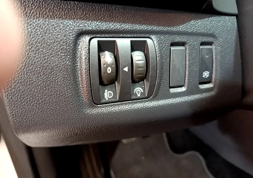 Gros plan sur les commandes de réglage des phares et de luminosité du tableau de bord dans une Renault Clio Business blanche de 2019.