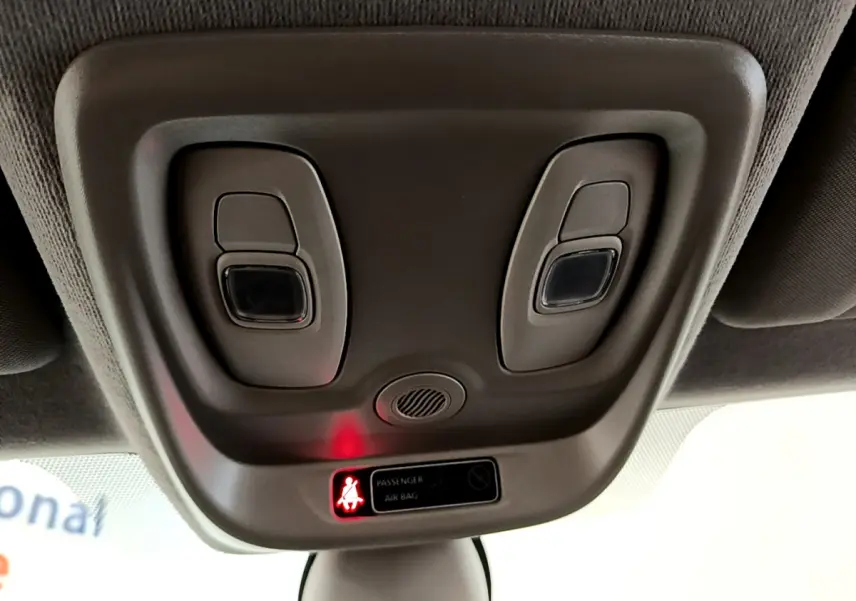 Vue rapprochée du plafonnier gris avec éclairages et témoin airbag passager allumé dans une Renault Clio blanche.
