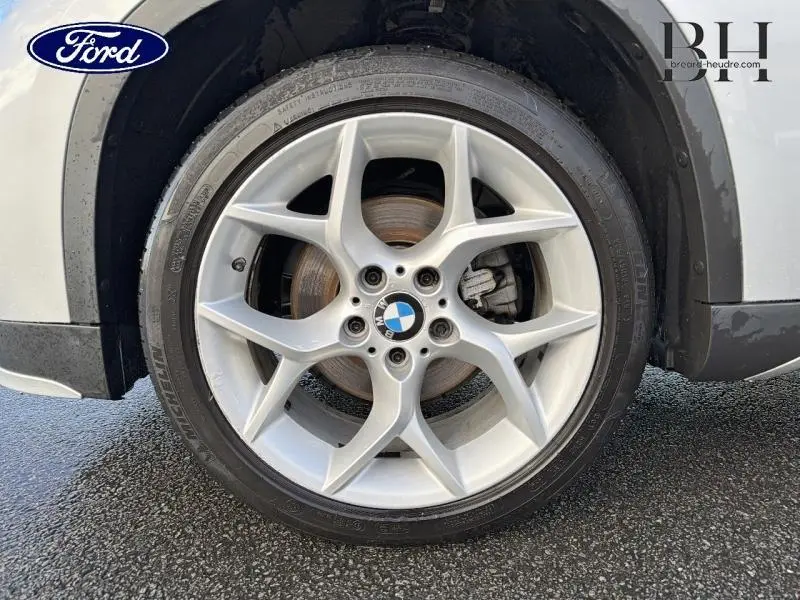 Gros plan sur la roue avant droite avec jante alu et logo BMW d'un X1 Mineralgrau de 2014
