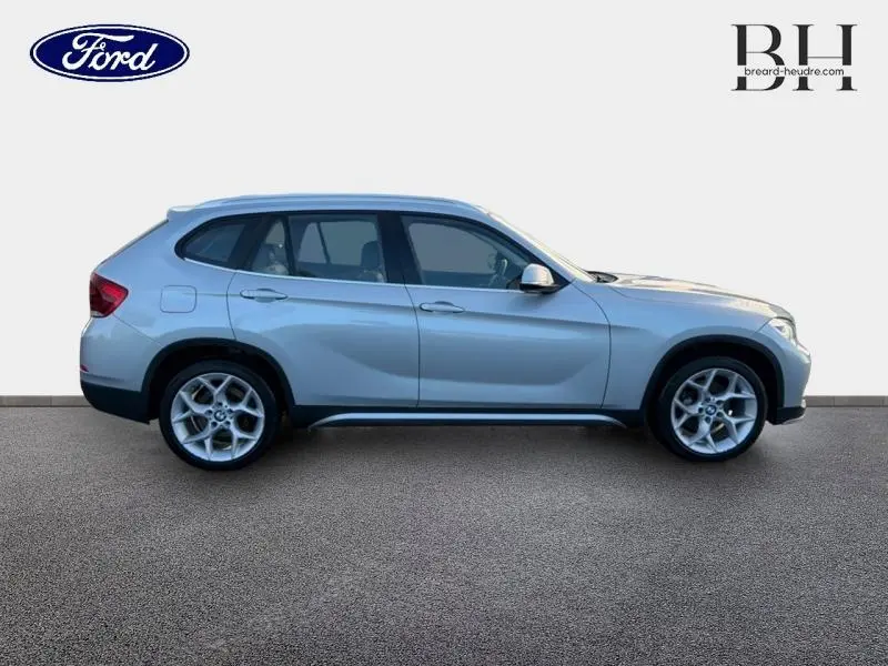 Profil côté gauche d'un BMW X1 xDrive25dA 2014 en Mineralgrau avec jantes alliage et lignes dynamiques.