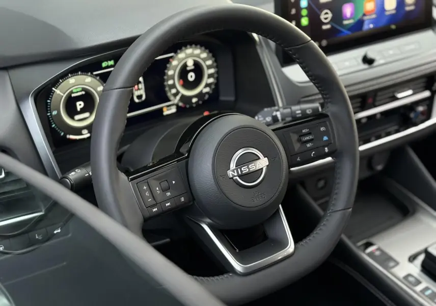 Vue intérieure rapprochée du volant cuir noir du Nissan Qashqai 2025 avec tableau de bord numérique et écran tactile.