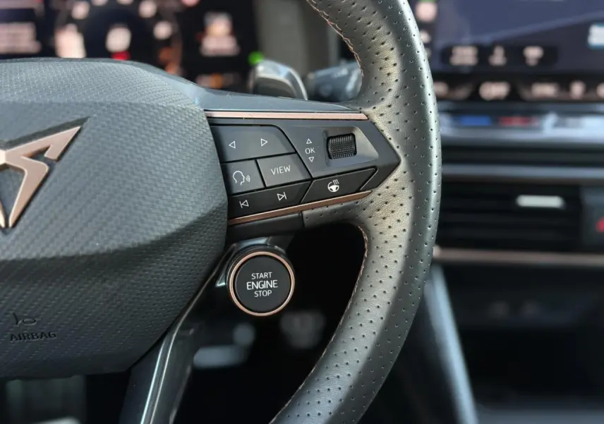 Gros plan sur le volant cuir perforé noir de la CUPRA Leon 2025 avec bouton start engine stop et commandes intégrées.