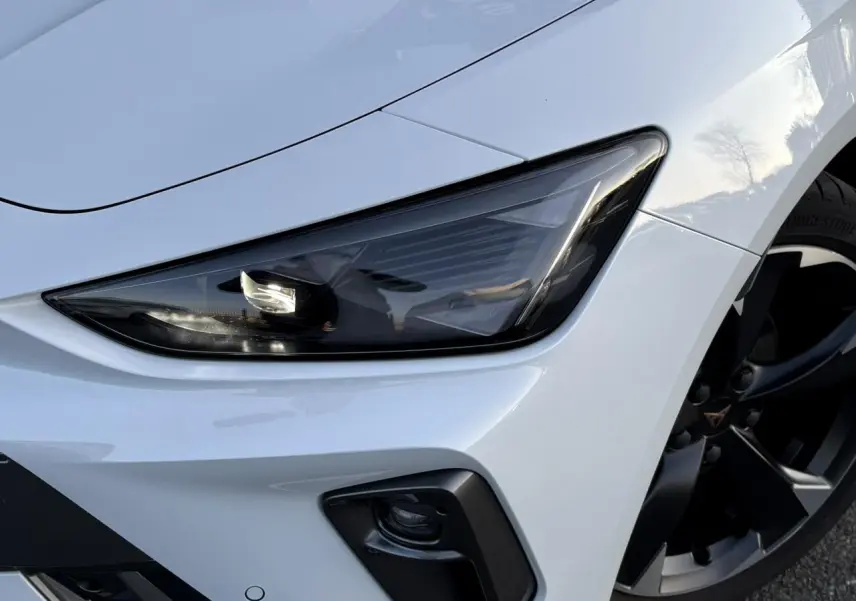 Gros plan sur le phare avant droit et la jante alliage noire d’une CUPRA Leon blanc neige.