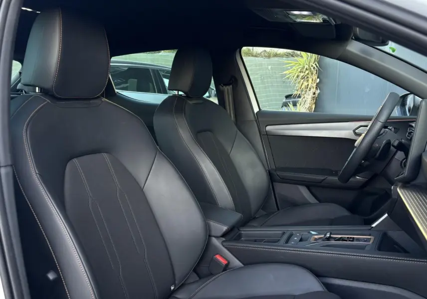 Vue intérieure côté conducteur de la CUPRA Leon 2025 avec sièges sport bimatière noirs et accoudoir central.