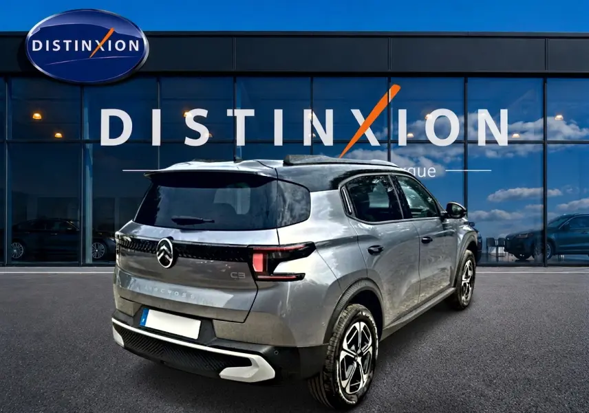 Vue 3/4 arrière droite d’un Citroën C3 Aircross gris mercury avec toit noir devant une vitrine Distinxion.