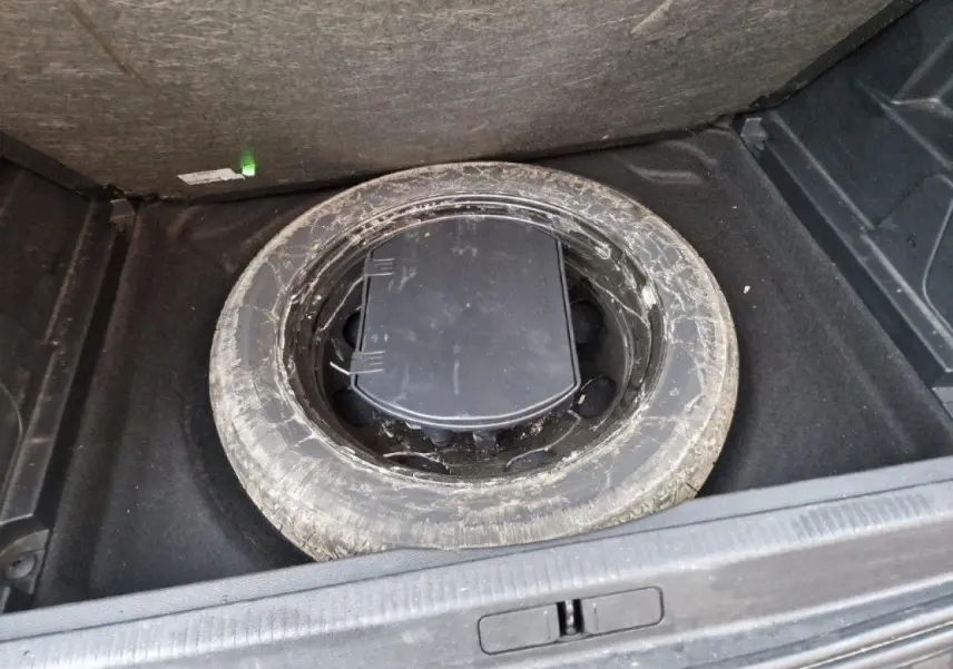 Vue plongeante sur la roue de secours usagée dans le coffre d'un Peugeot 3008 noir 2019.