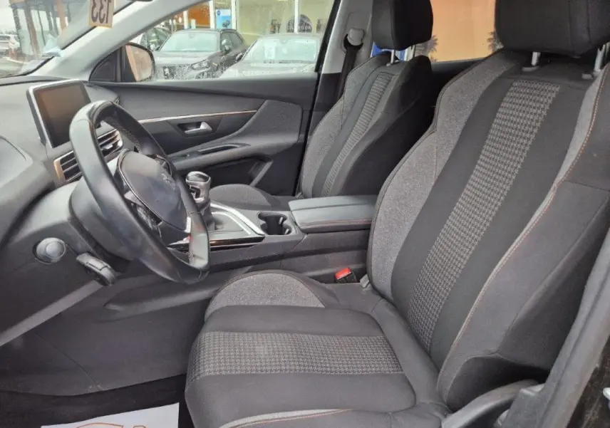 Intérieur avant du Peugeot 3008 noir 2019, sièges tissu gris et noir avec surpiqûres orange, volant cuir multifonctions.