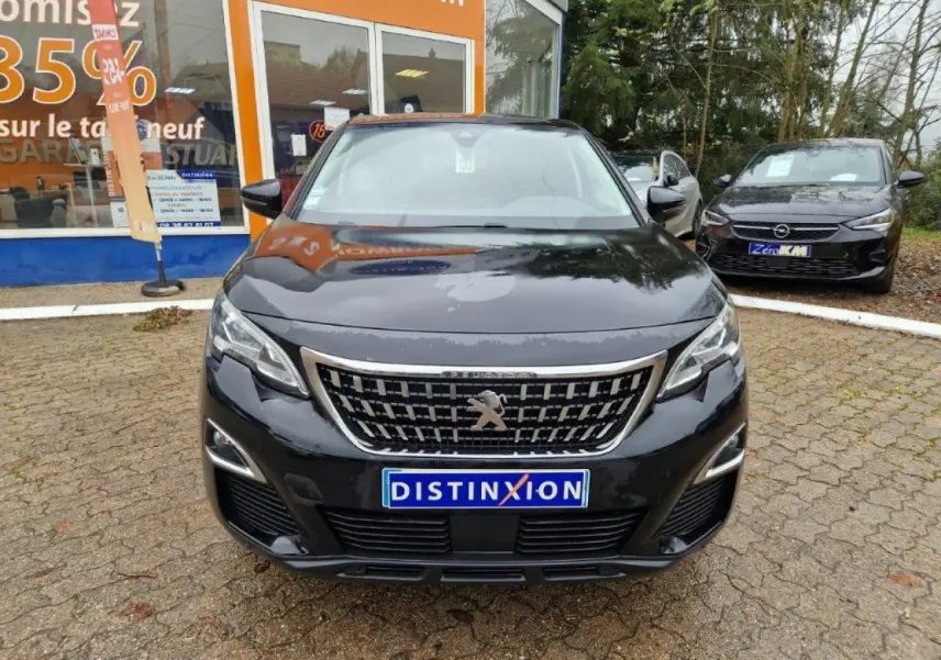 Vue de face d'un Peugeot 3008 noir 2019 avec calandre chromée et plaque Distinxion devant un showroom.