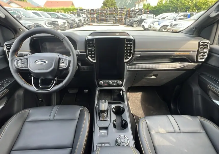 Vue intérieure frontale du Ford Ranger 2.3 PHEV Wildtrak Plus 2025 avec tableau de bord noir et coutures orange contrastantes.