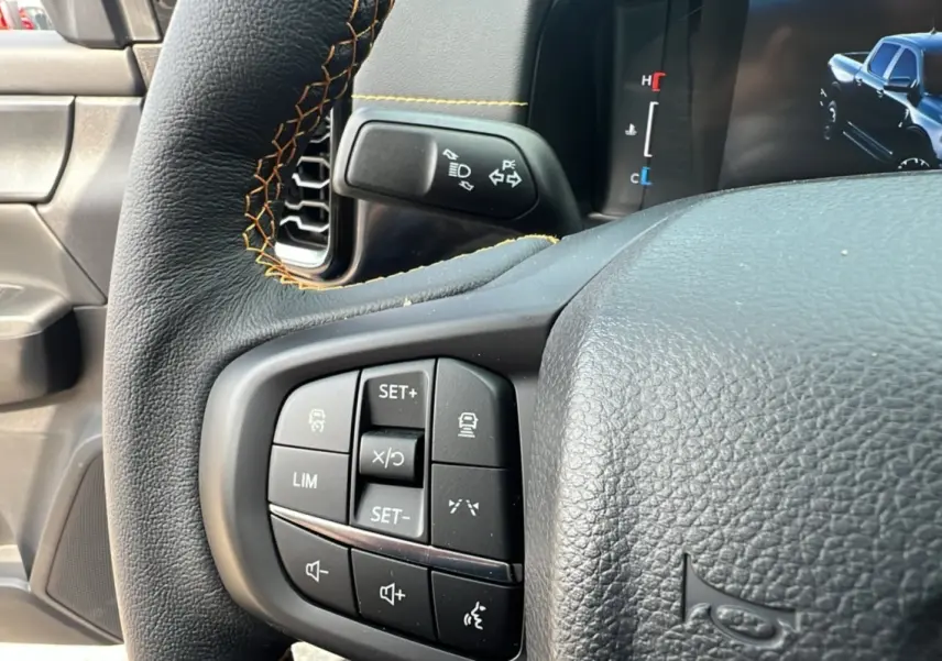 Gros plan sur le volant du Ford Ranger 2025 noir agate, avec commandes intégrées et coutures orange visibles.