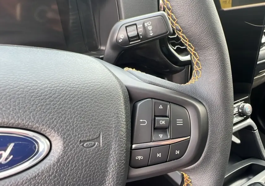 Gros plan sur le volant du Ford Ranger 2025 noir agate, avec surpiqûres orange et commandes intégrées au volant.