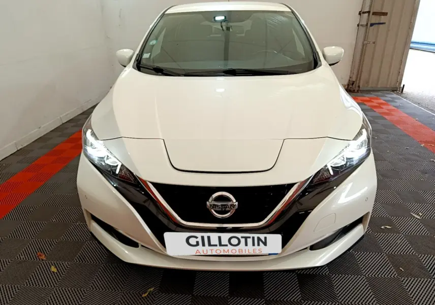 Vue avant d'une Nissan LEAF blanche 2020 avec phares LED allumés et calandre noire brillante.