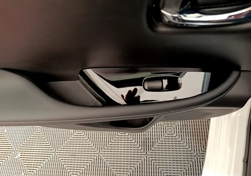 Poignée intérieure noire côté gauche de la porte avant d'une Nissan Leaf blanche, avec reflet visible sur la surface brillante.