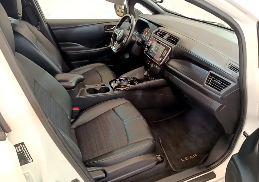Intérieur avant droit du Nissan Leaf blanc 2020, sièges noirs, tableau de bord avec écran tactile et volant cuir.