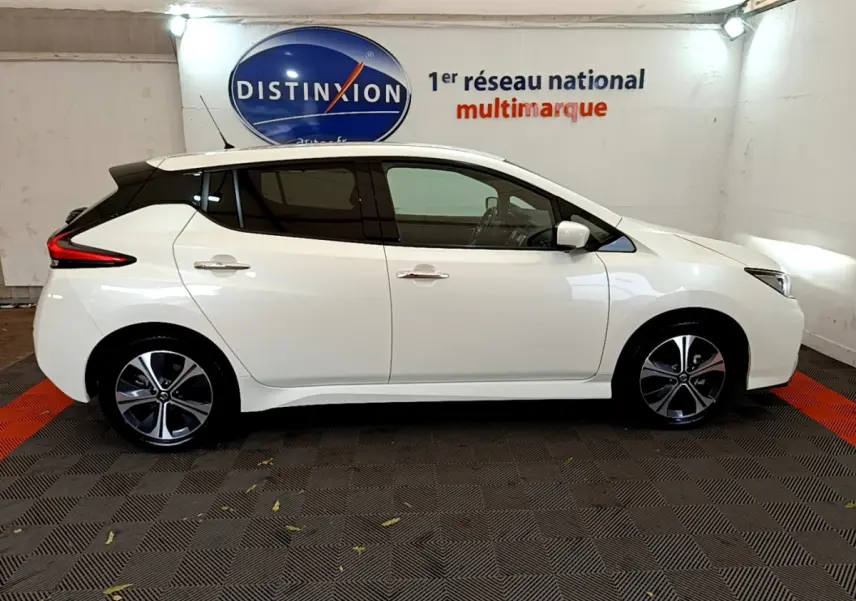 Profil côté gauche d'une Nissan Leaf électrique blanche 2020, avec jantes modernes et vitres teintées, en intérieur showroom.