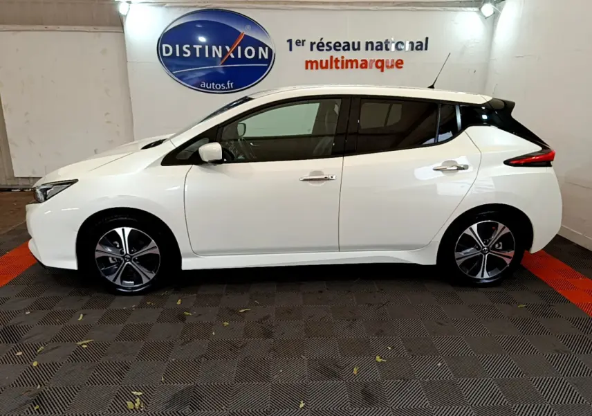 Profil droit d'une Nissan Leaf blanche 2020 avec toit noir et jantes alliage bicolores dans un showroom.