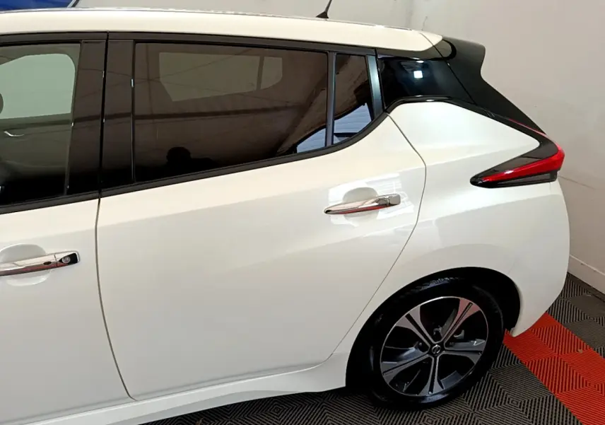Vue côté droit arrière d'une Nissan Leaf blanche avec toit noir et feux arrière profilés en intérieur showroom.