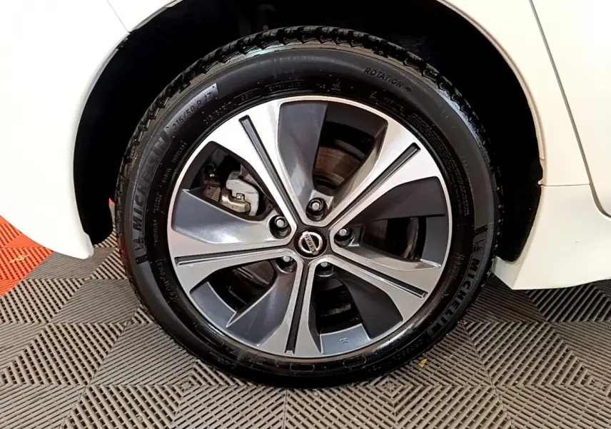 Gros plan sur la roue avant droite d'une Nissan Leaf blanche avec jante alliage bicolore et logo Nissan au centre.