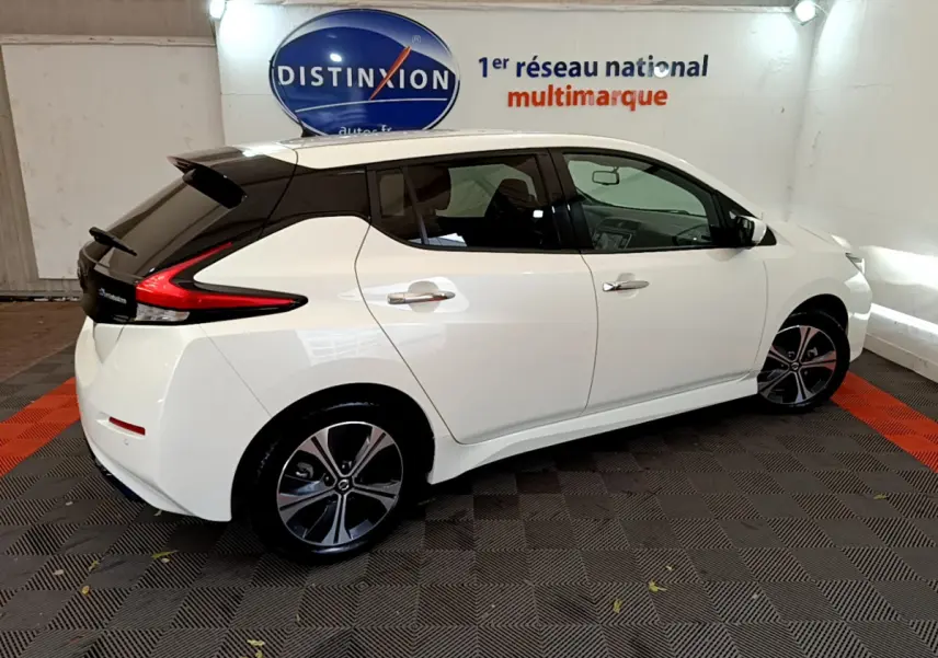 Vue 3/4 arrière droite d'une Nissan Leaf blanche avec toit noir et jantes alliage dans un showroom intérieur.