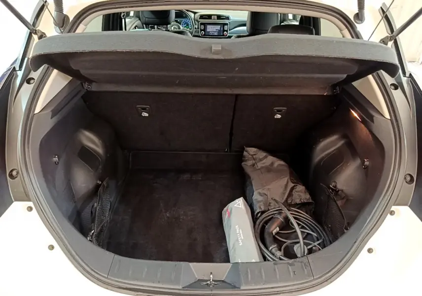 Coffre ouvert d'une Nissan Leaf blanche 2020, vue arrière montrant câble de recharge et tablette de séparation.