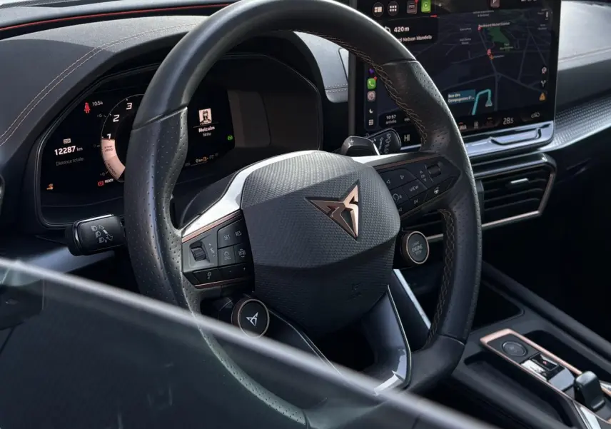 Vue rapprochée du volant noir perforé Cupra avec commandes intégrées et écran tactile de navigation à droite.