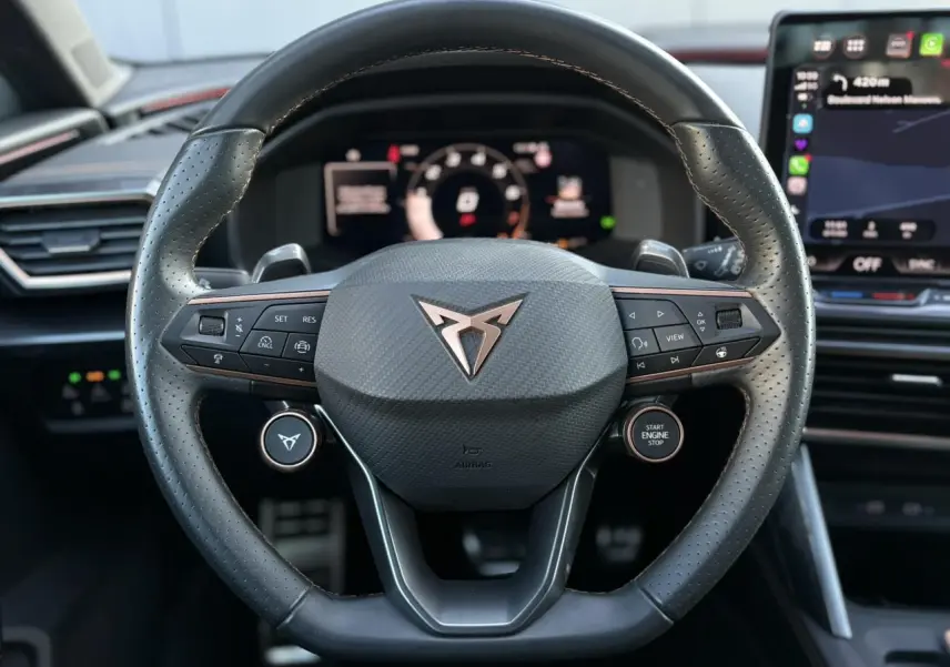 Vue rapprochée du volant cuir perforé noir avec logo CUPRA et commandes multifonctions du Leon 1.5 e-TSI 2025.