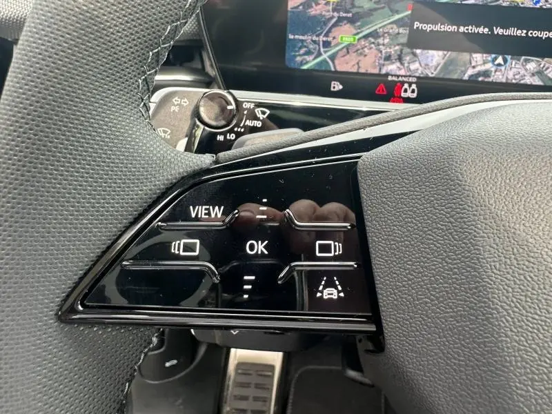 Gros plan sur les commandes au volant côté gauche de l'Audi Q3 gris 2026, avec affichage numérique en arrière-plan.