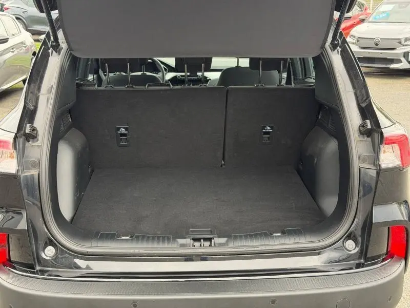 Vue arrière du coffre ouvert du Ford Kuga 1.5 EcoBoost 150ch Titanium 2024 noir, montrant un espace de chargement vide et propre.