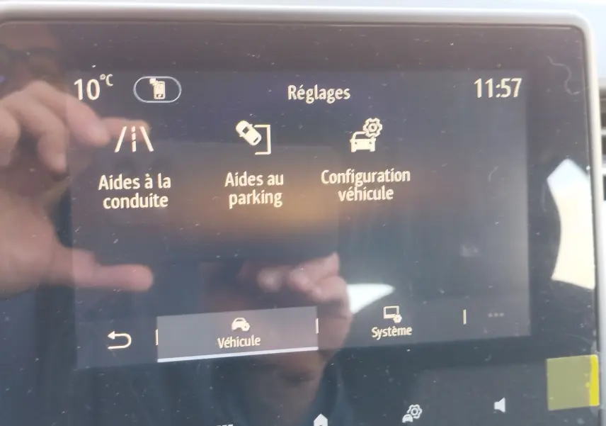 Écran tactile du tableau de bord de la Renault Clio 1.6 E-Tech noir, affichant les réglages d’aides à la conduite et au parking.