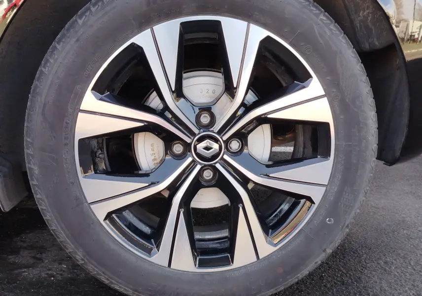 Gros plan sur la jante alliage bicolore noire et argent avec logo Renault au centre, roue avant droite du Renault Clio noir étoile.